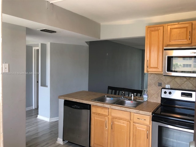 kitchen with light brown cabinets, backsplash, sink, light hardwood / wood-style flooring, and appliances with stainless steel finishes