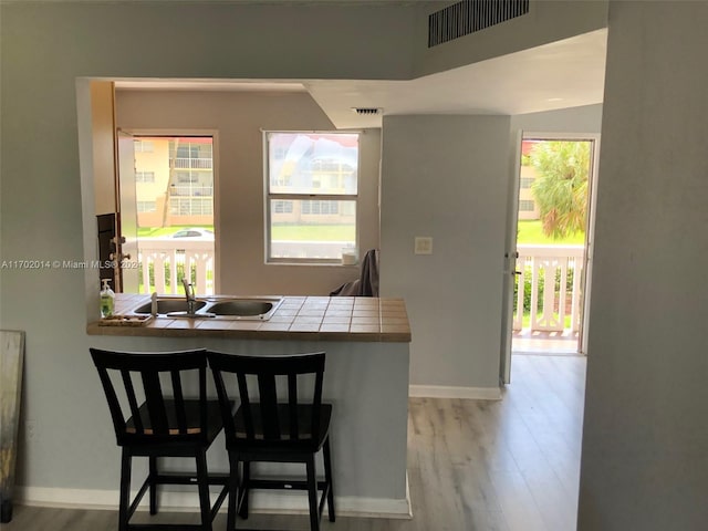 kitchen with a kitchen bar, tile counters, light hardwood / wood-style flooring, and sink