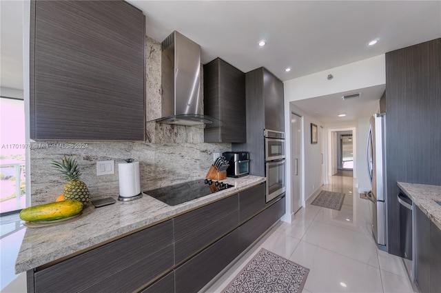 kitchen featuring light stone countertops, tasteful backsplash, stainless steel appliances, wall chimney range hood, and light tile patterned floors