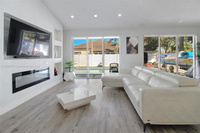 living room with built in shelves, light hardwood / wood-style flooring, and lofted ceiling