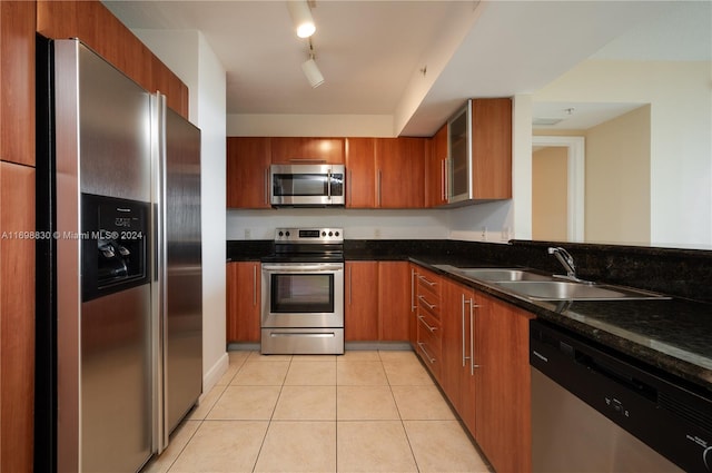 kitchen featuring sink, stainless steel appliances, dark stone counters, track lighting, and light tile patterned floors