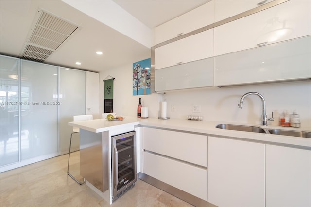 kitchen featuring kitchen peninsula, white cabinetry, beverage cooler, and sink