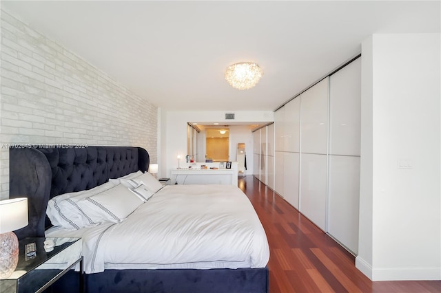 bedroom featuring dark hardwood / wood-style flooring and brick wall