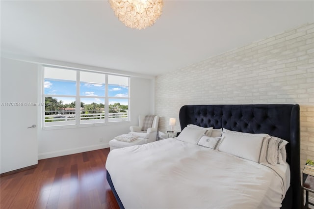 bedroom featuring dark hardwood / wood-style flooring, an inviting chandelier, and brick wall