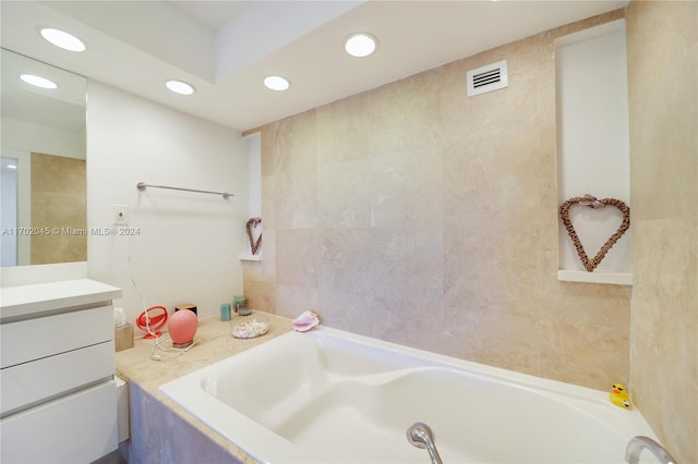 bathroom featuring tiled tub, vanity, and tile walls