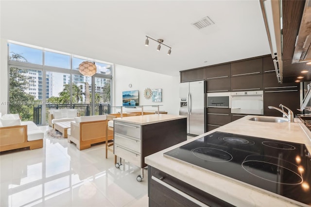 kitchen with white oven, black electric stovetop, sink, stainless steel refrigerator with ice dispenser, and dark brown cabinetry