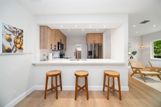 kitchen with stainless steel fridge, light wood-type flooring, a breakfast bar area, and sink