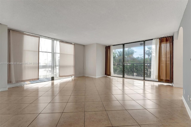 empty room with floor to ceiling windows, light tile patterned floors, and a textured ceiling