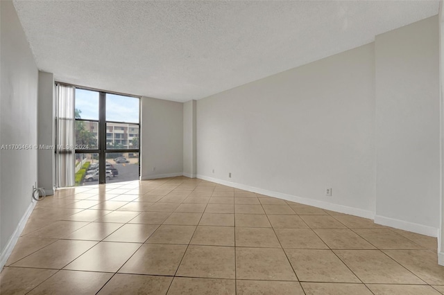 empty room with a wall of windows, light tile patterned floors, and a textured ceiling