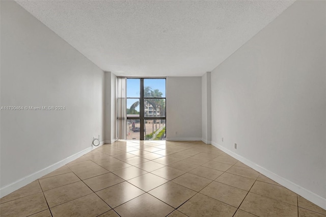 tiled empty room featuring a textured ceiling and floor to ceiling windows