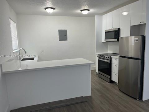 kitchen with sink, stainless steel appliances, dark hardwood / wood-style flooring, kitchen peninsula, and white cabinets