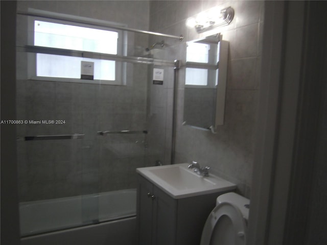 full bathroom with a wealth of natural light, vanity, bath / shower combo with glass door, and toilet