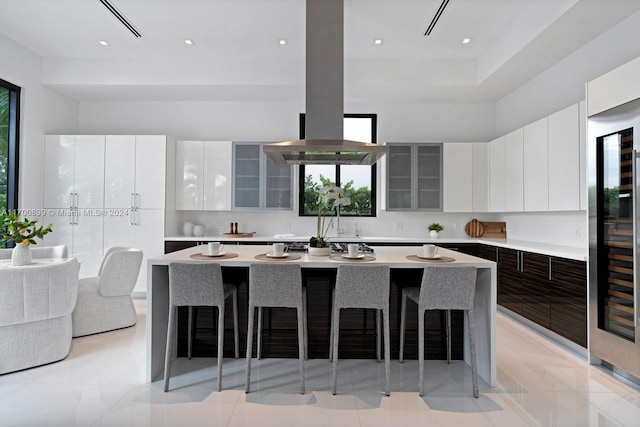 kitchen featuring light tile patterned floors, a kitchen island, island range hood, a breakfast bar, and white cabinets