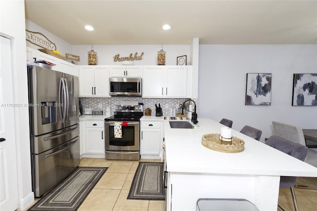 kitchen with white cabinetry, stainless steel appliances, a kitchen breakfast bar, decorative backsplash, and light tile patterned floors