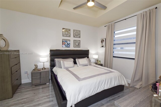 bedroom featuring a raised ceiling, ceiling fan, and light hardwood / wood-style floors