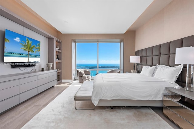 bedroom with light hardwood / wood-style floors and a water view