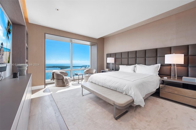 bedroom with hardwood / wood-style flooring, a water view, and access to outside