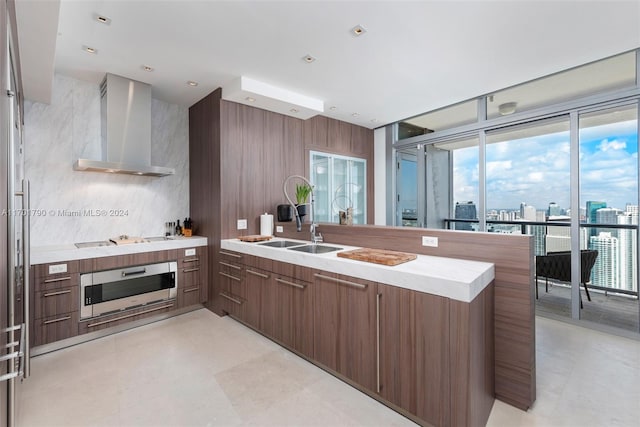 kitchen with stainless steel oven, wall chimney range hood, sink, stovetop, and kitchen peninsula