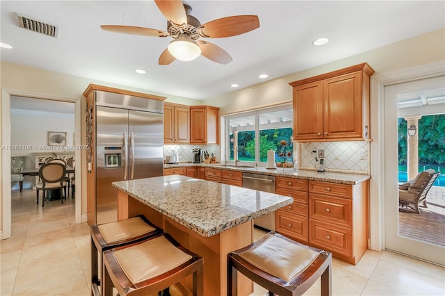 kitchen with visible vents, light stone counters, a kitchen breakfast bar, a center island, and stainless steel appliances