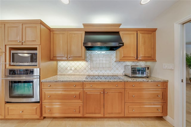 kitchen featuring light stone counters, a toaster, backsplash, appliances with stainless steel finishes, and wall chimney exhaust hood