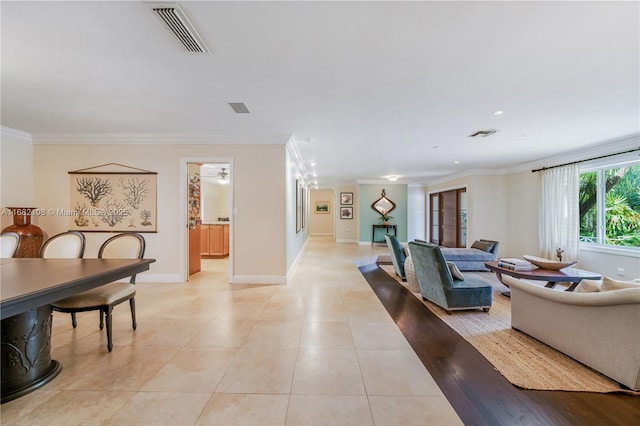 living area featuring light tile patterned floors, baseboards, visible vents, and ornamental molding