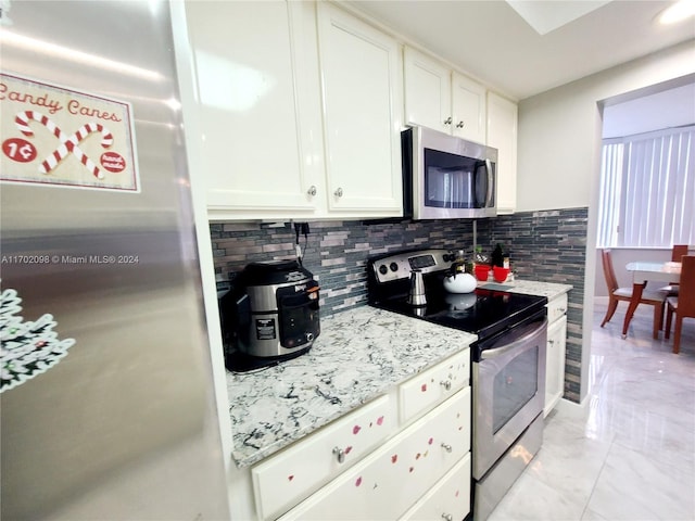 kitchen featuring white cabinets, appliances with stainless steel finishes, tasteful backsplash, and light stone counters