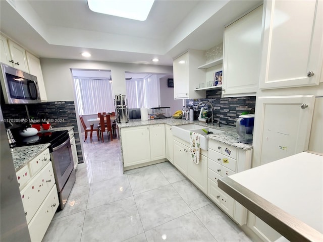 kitchen with sink, backsplash, a tray ceiling, white cabinets, and appliances with stainless steel finishes