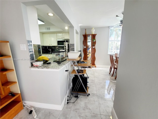 kitchen featuring kitchen peninsula, backsplash, light stone counters, ceiling fan, and white cabinetry