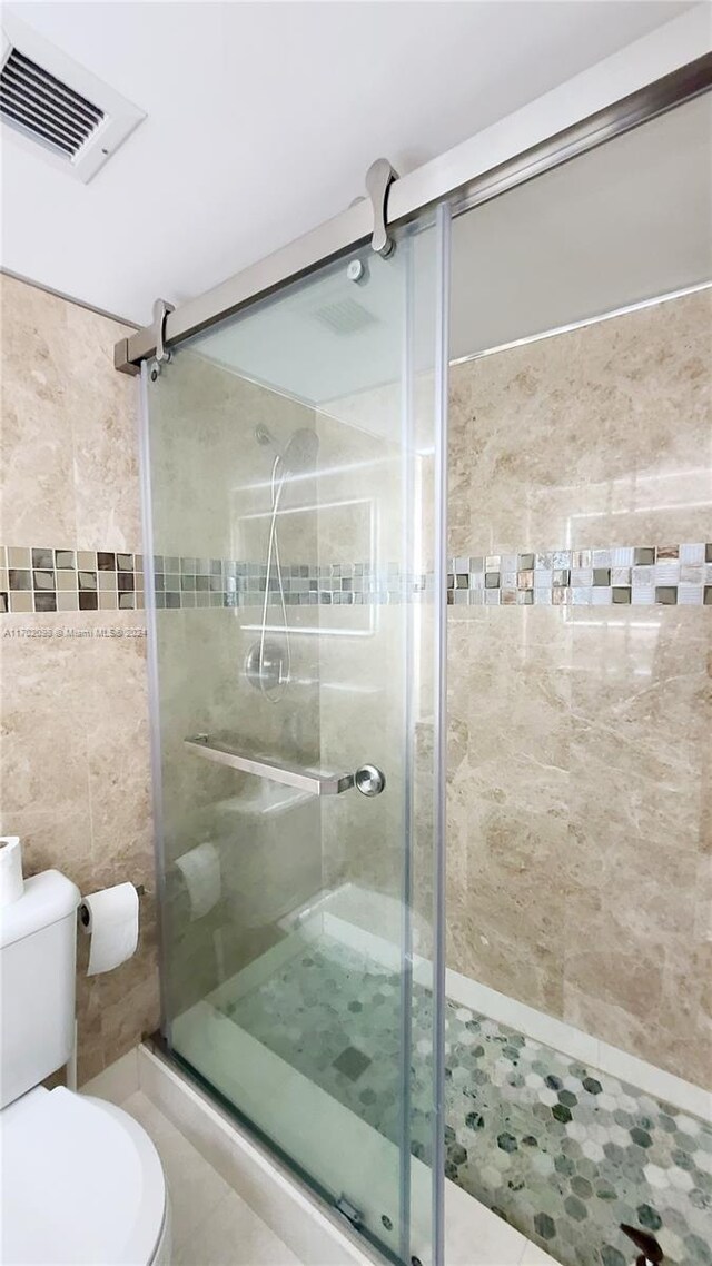 bathroom featuring tile patterned floors, a shower with shower door, and toilet