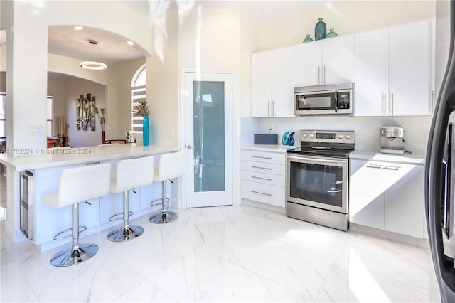 kitchen with a kitchen bar, kitchen peninsula, stainless steel appliances, and white cabinetry