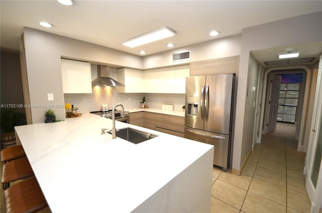 kitchen featuring light countertops, a peninsula, stainless steel fridge with ice dispenser, and wall chimney range hood