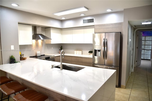 kitchen with stainless steel appliances, a sink, wall chimney range hood, a peninsula, and a kitchen bar