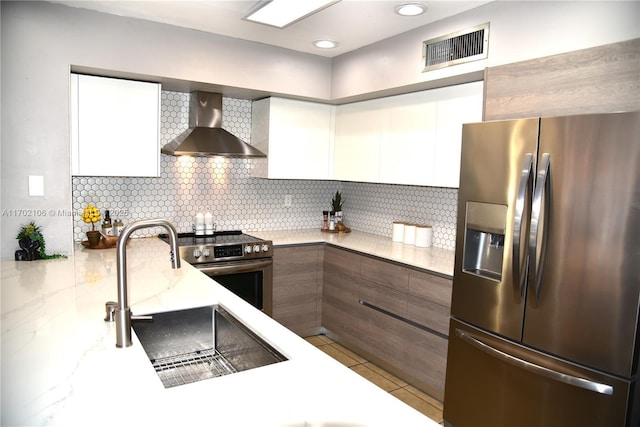 kitchen with stainless steel appliances, wall chimney exhaust hood, light countertops, and white cabinets