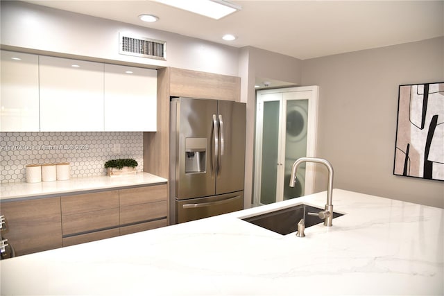 kitchen with light stone counters, a sink, stainless steel fridge with ice dispenser, and modern cabinets