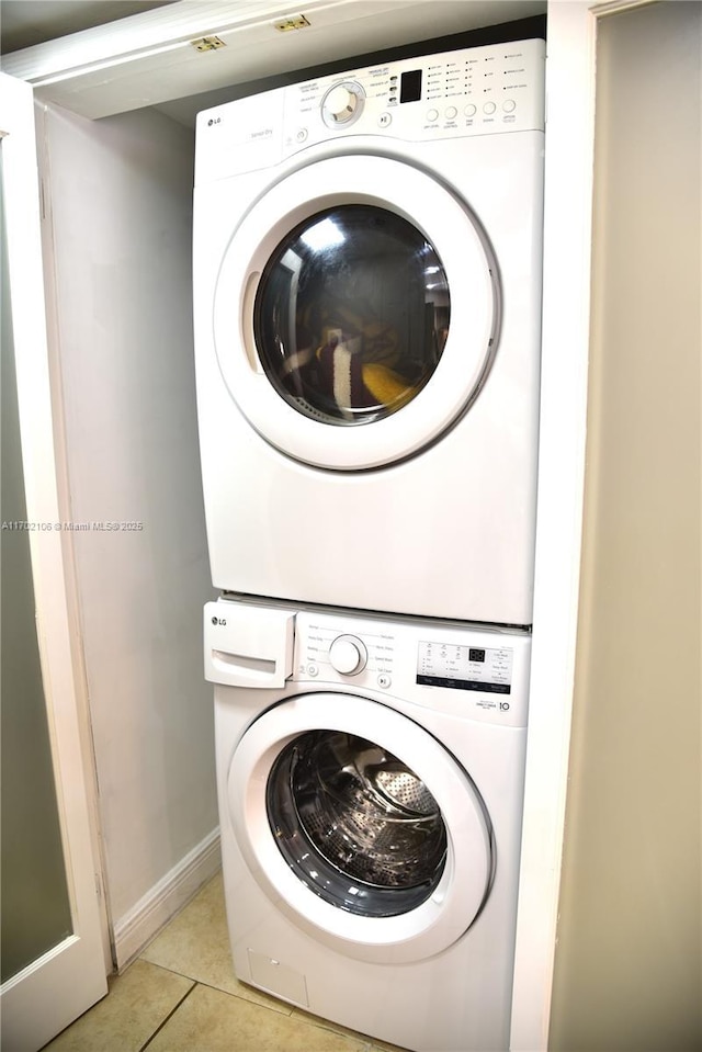 washroom featuring laundry area, light tile patterned flooring, and stacked washer / drying machine