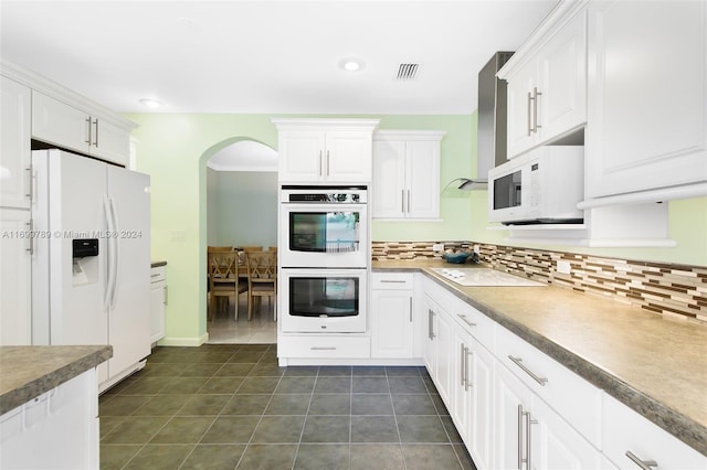 kitchen with tasteful backsplash, white cabinets, dark tile patterned flooring, and white appliances