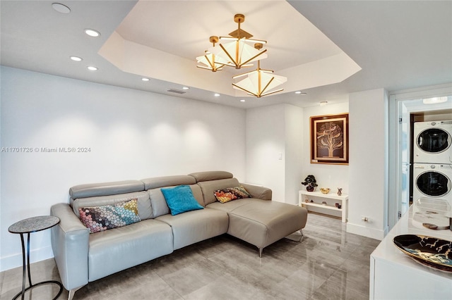 living room with a chandelier, a tray ceiling, and stacked washer and clothes dryer