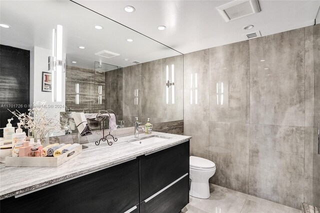 bathroom featuring walk in shower, vanity, toilet, and tile walls