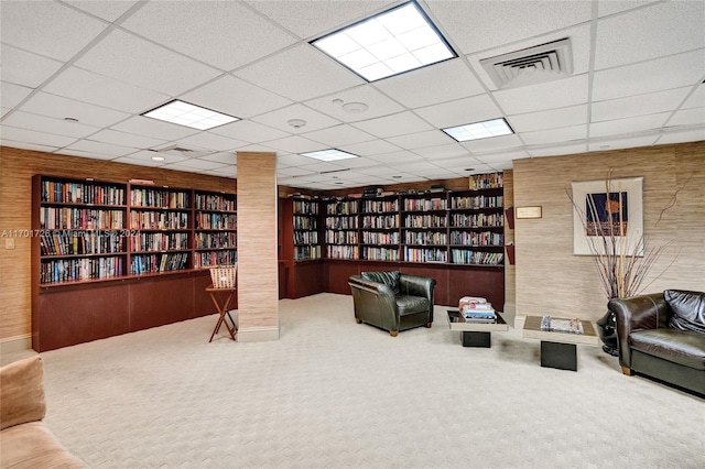 living area with wooden walls, a drop ceiling, and carpet floors