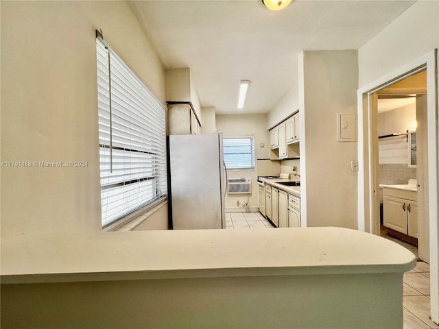 kitchen with electric range, light tile patterned flooring, kitchen peninsula, stainless steel fridge, and white cabinets