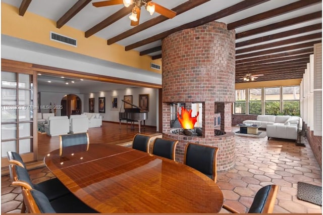 dining area with beamed ceiling, a fireplace, and ceiling fan