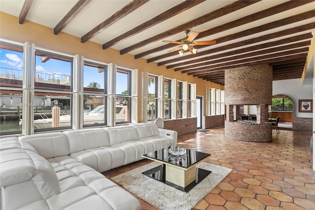 living room featuring beamed ceiling, a multi sided fireplace, a healthy amount of sunlight, and ceiling fan