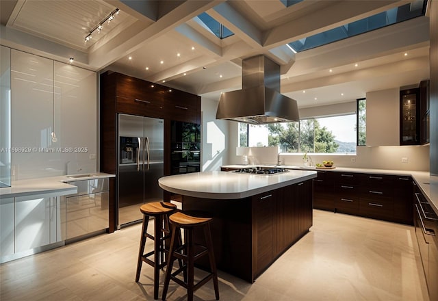 kitchen with a breakfast bar, island range hood, dark brown cabinets, a kitchen island, and stainless steel appliances