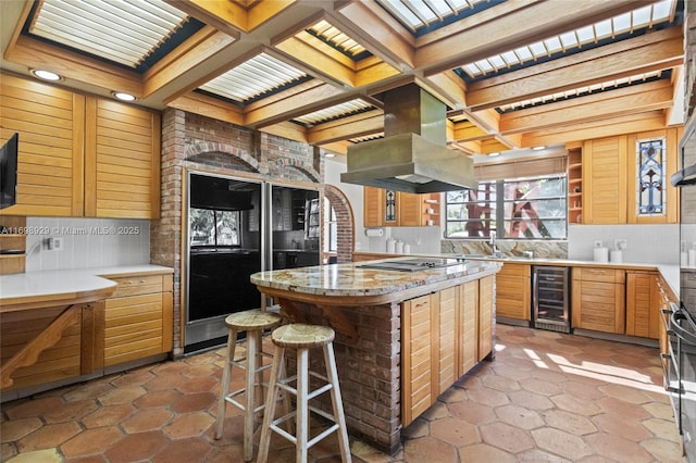 kitchen with refrigerator, beverage cooler, island exhaust hood, coffered ceiling, and a center island