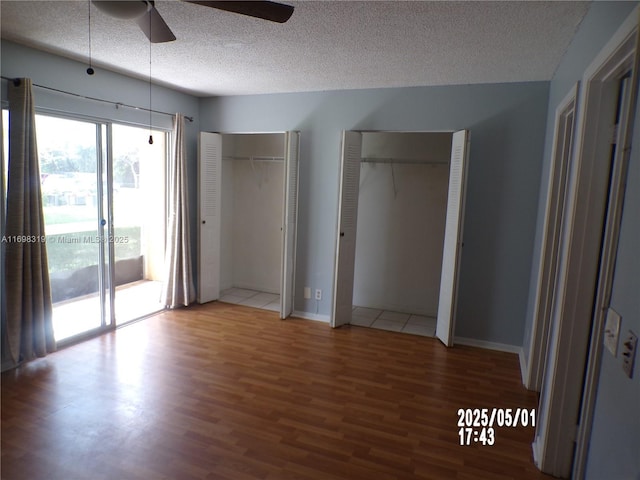 unfurnished bedroom featuring ceiling fan, a textured ceiling, wood finished floors, two closets, and access to outside