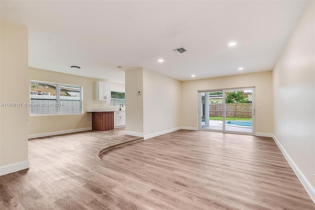 unfurnished living room with sink, a wealth of natural light, and light hardwood / wood-style flooring