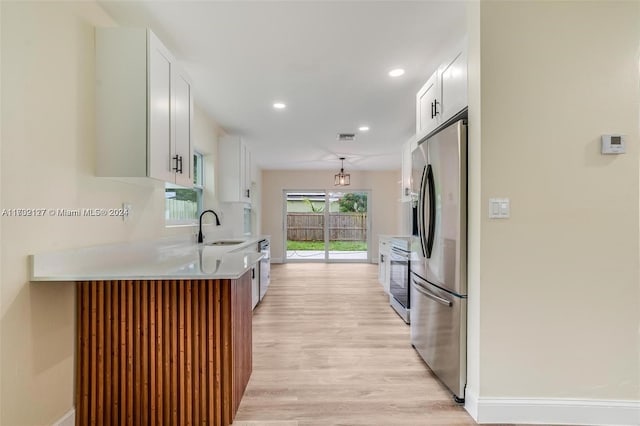 kitchen with sink, hanging light fixtures, stainless steel appliances, light hardwood / wood-style floors, and white cabinets