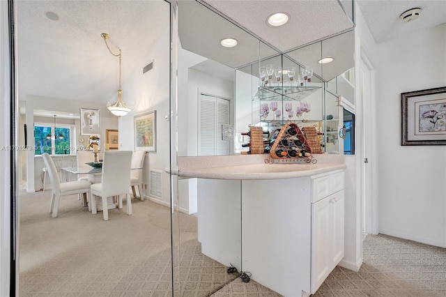 kitchen with white cabinets, light colored carpet, a textured ceiling, and hanging light fixtures