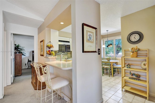 kitchen with a notable chandelier, sink, a textured ceiling, decorative light fixtures, and light colored carpet