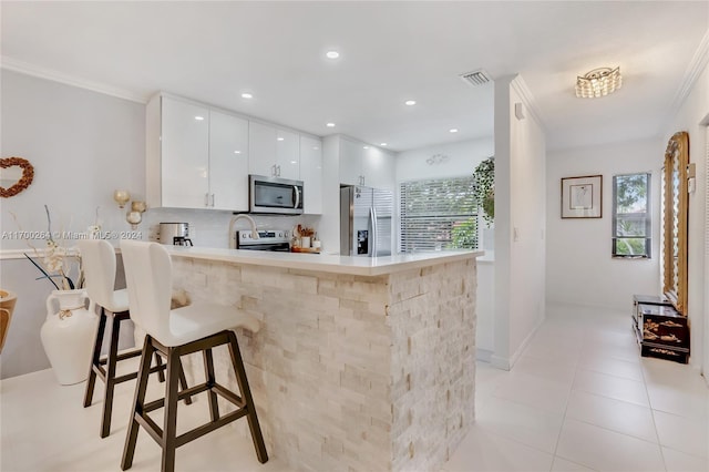 kitchen featuring white cabinets, a kitchen bar, kitchen peninsula, and stainless steel appliances